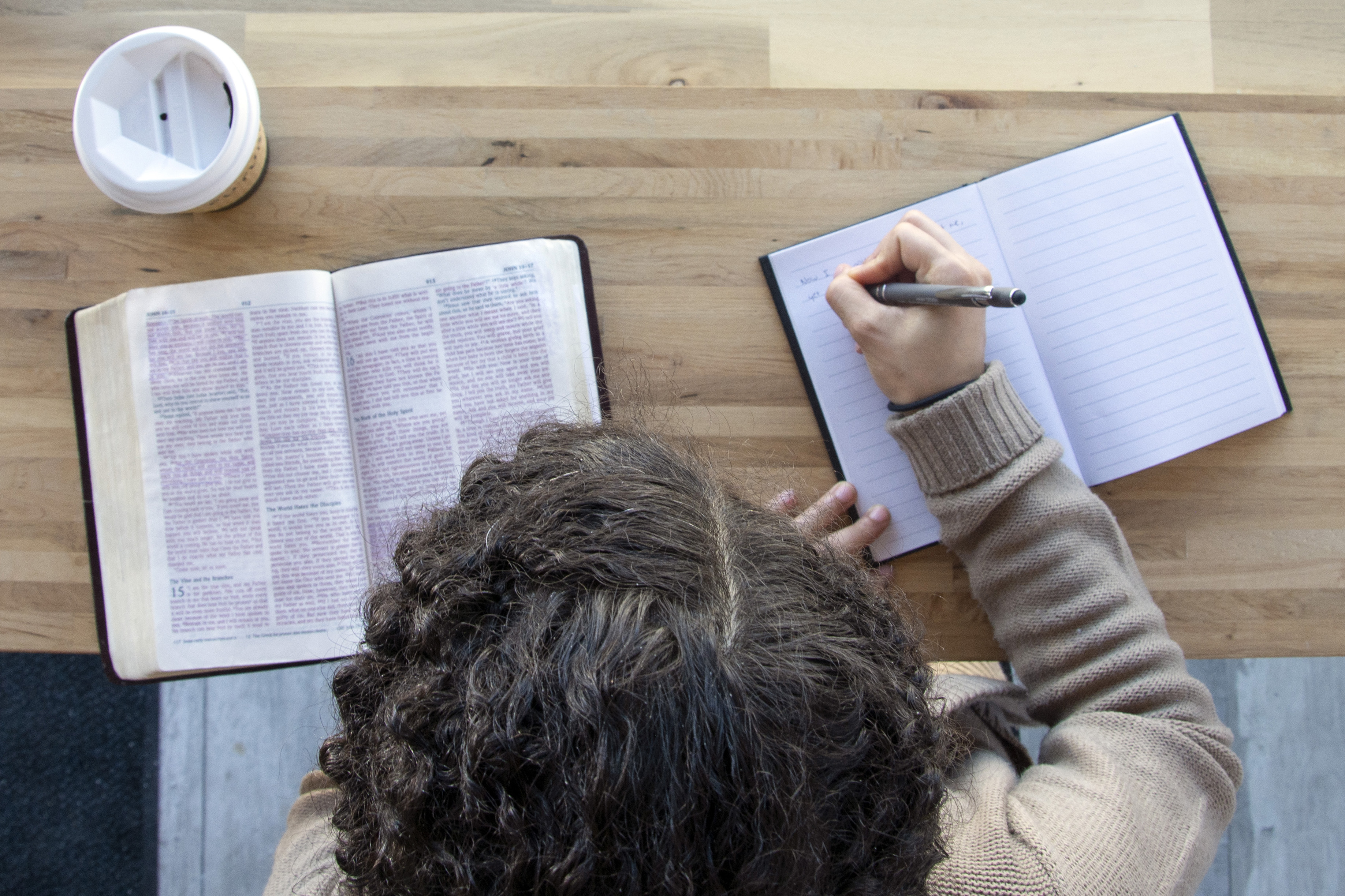 black woman sits and studying her bible with journal while drinking coffee