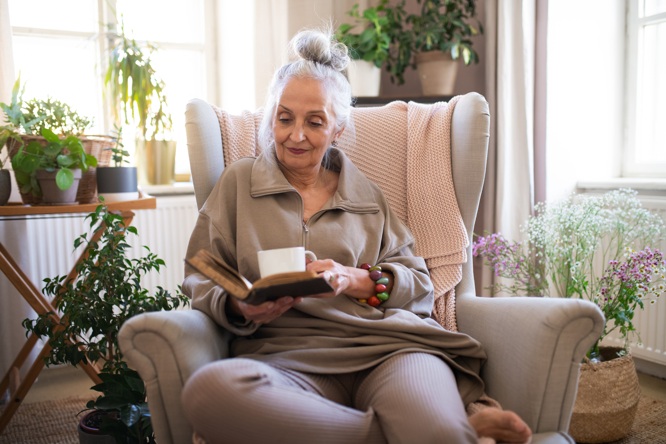 Relaxed senior woman sitting in armchair and reading book indoors at home.