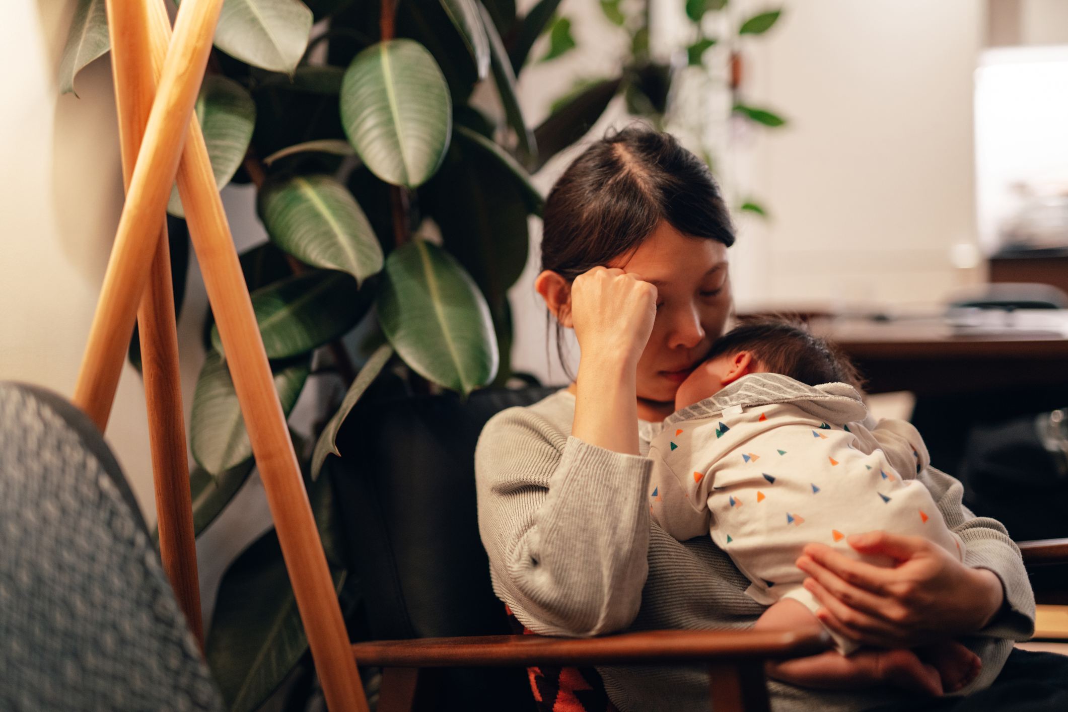 Tired Asian mother falling asleep while holding her baby to sleep at night.