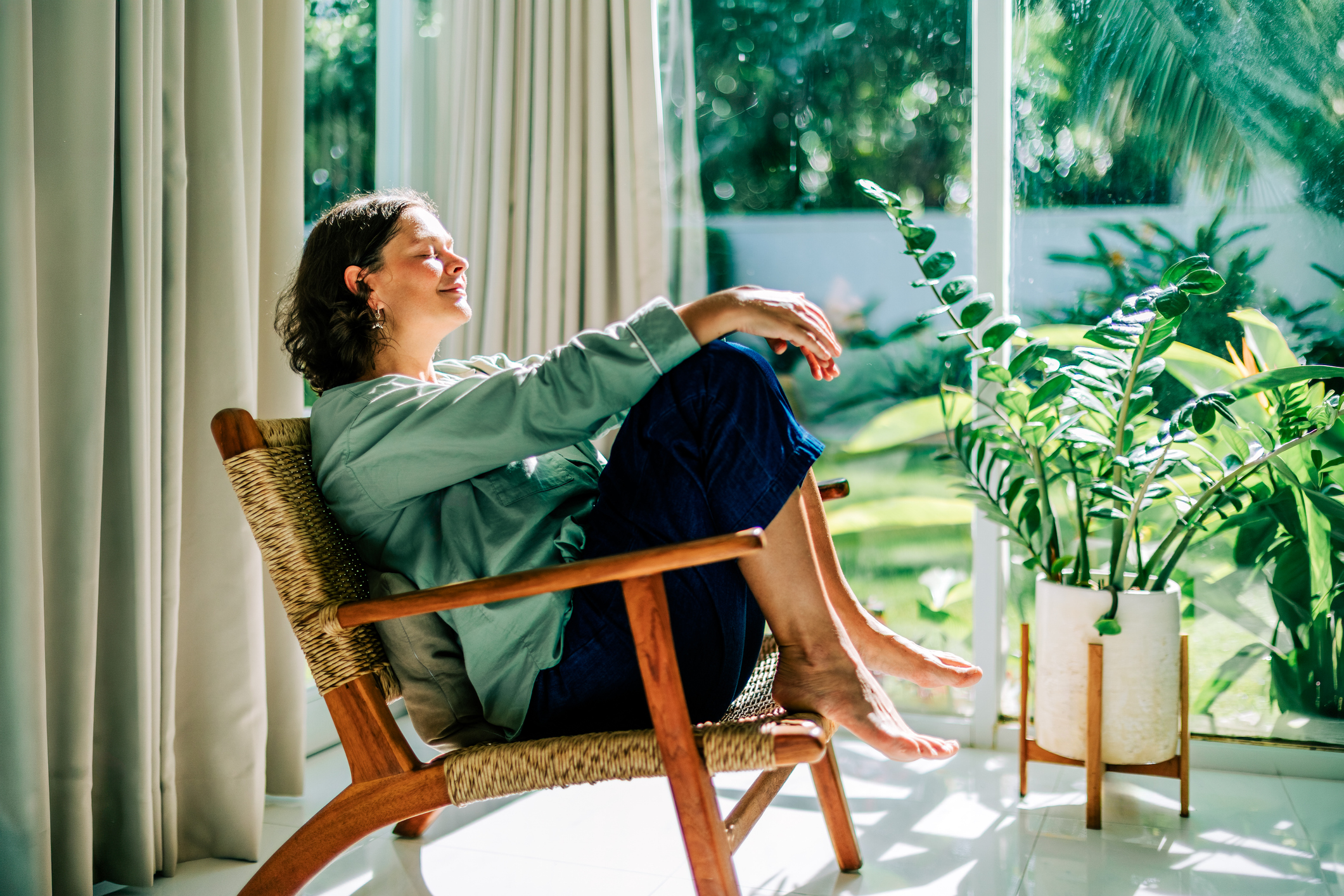 Woman relaxing in armchair by window enjoying morning sun