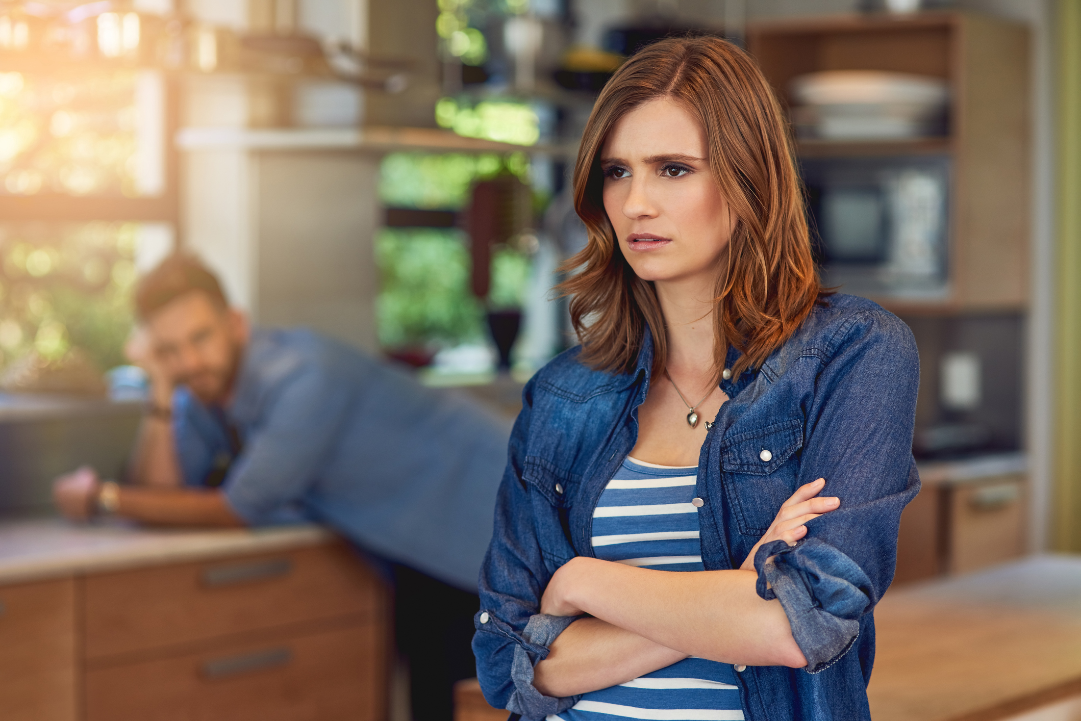 Shot of a young woman looking upset after a fight with her husband who is standing in the background