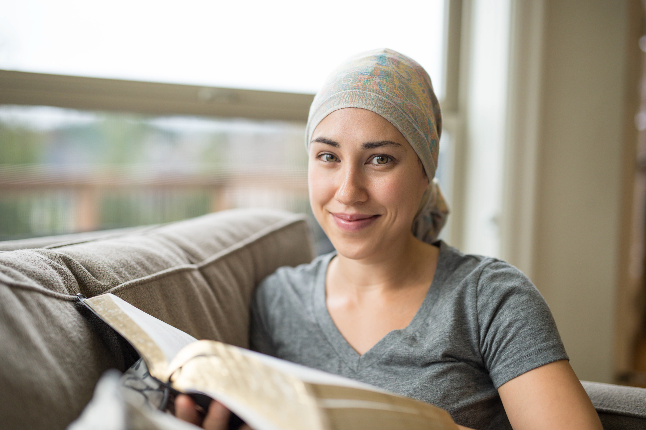 An ethnic young female adult with cancer is reading the Bible inside her home